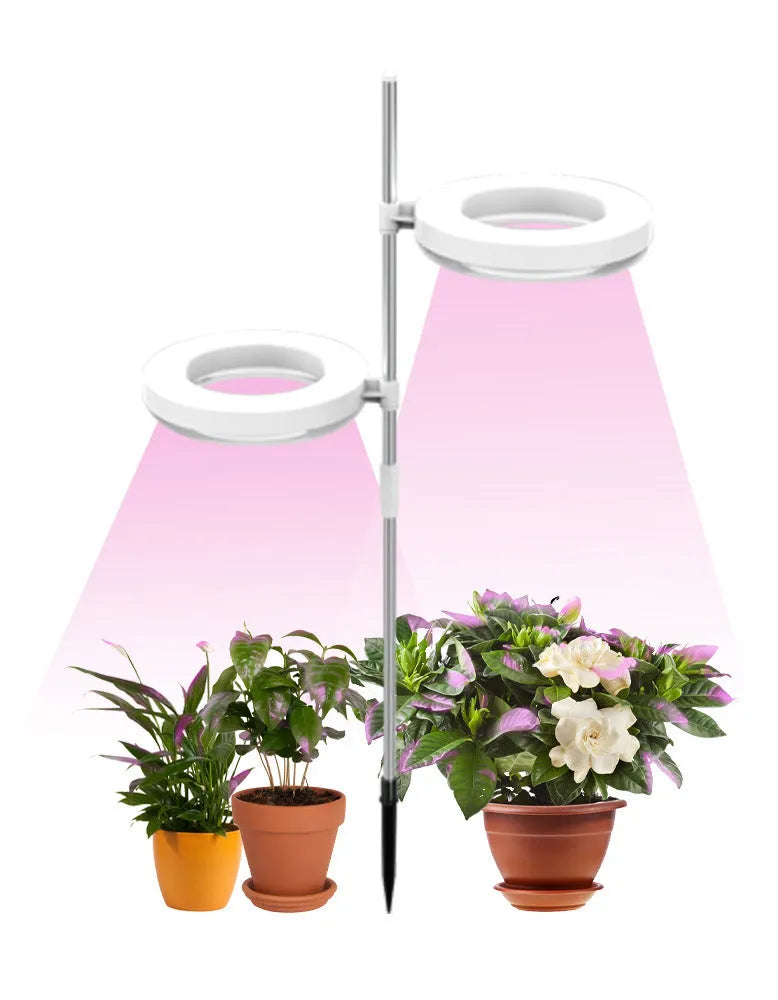 A compact LED plant growth light with a double-headed design, resting beside a small potted plant on a desk.