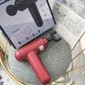 A grey handheld fascia gun muscle massager on a plain background.