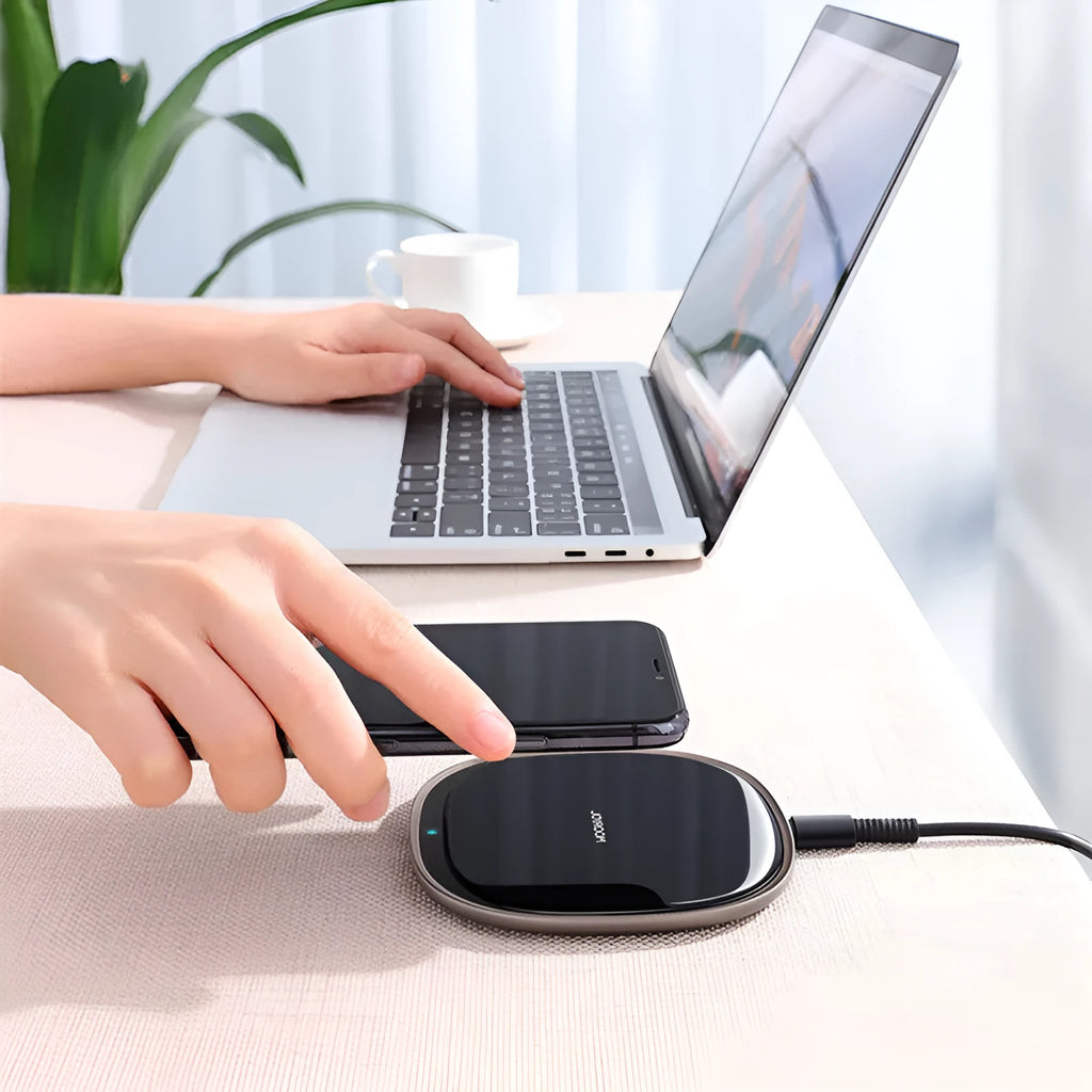 Black 15W Qi wireless fast charger with zinc alloy frame and glass top on a desk.