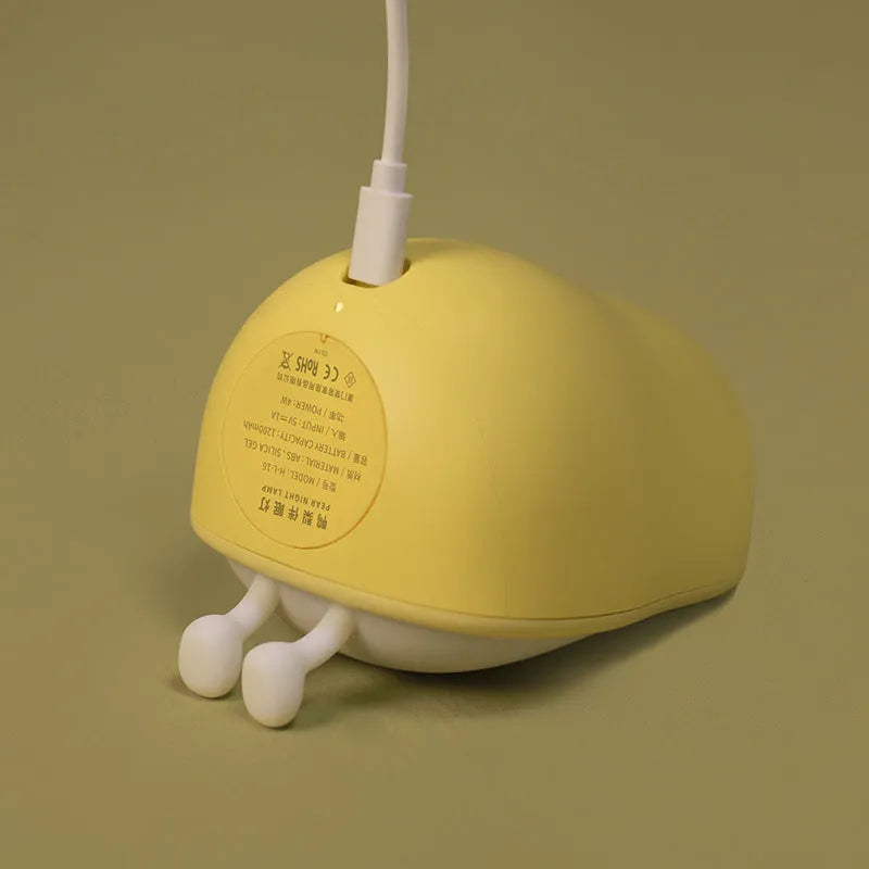 Pear-shaped silicone night light with warm yellow glow on a bedside table.