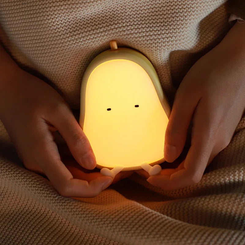Pear-shaped silicone night light with warm yellow glow on a bedside table.