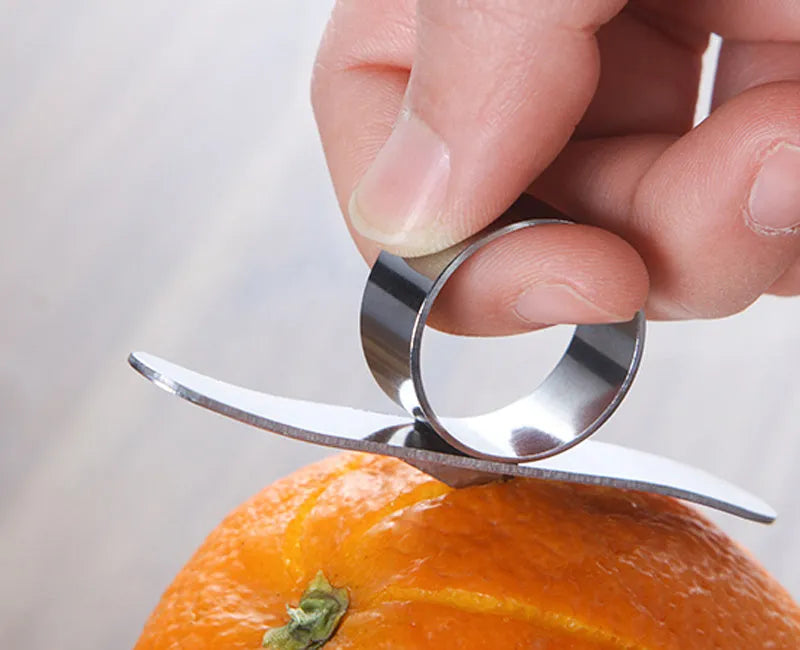 Silver stainless steel fruit peeler ring for oranges, citrus, and pomegranates on a kitchen surface.