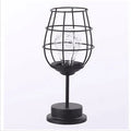 Minimalist hollow wrought iron table lamp in red wine bottle shape with warm white light on a desk