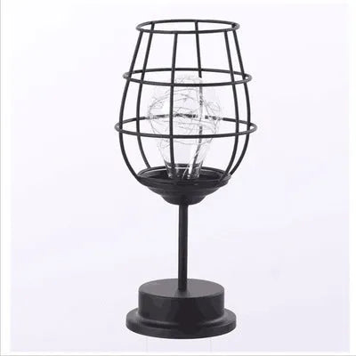Minimalist hollow wrought iron table lamp in red wine bottle shape with warm white light on a desk