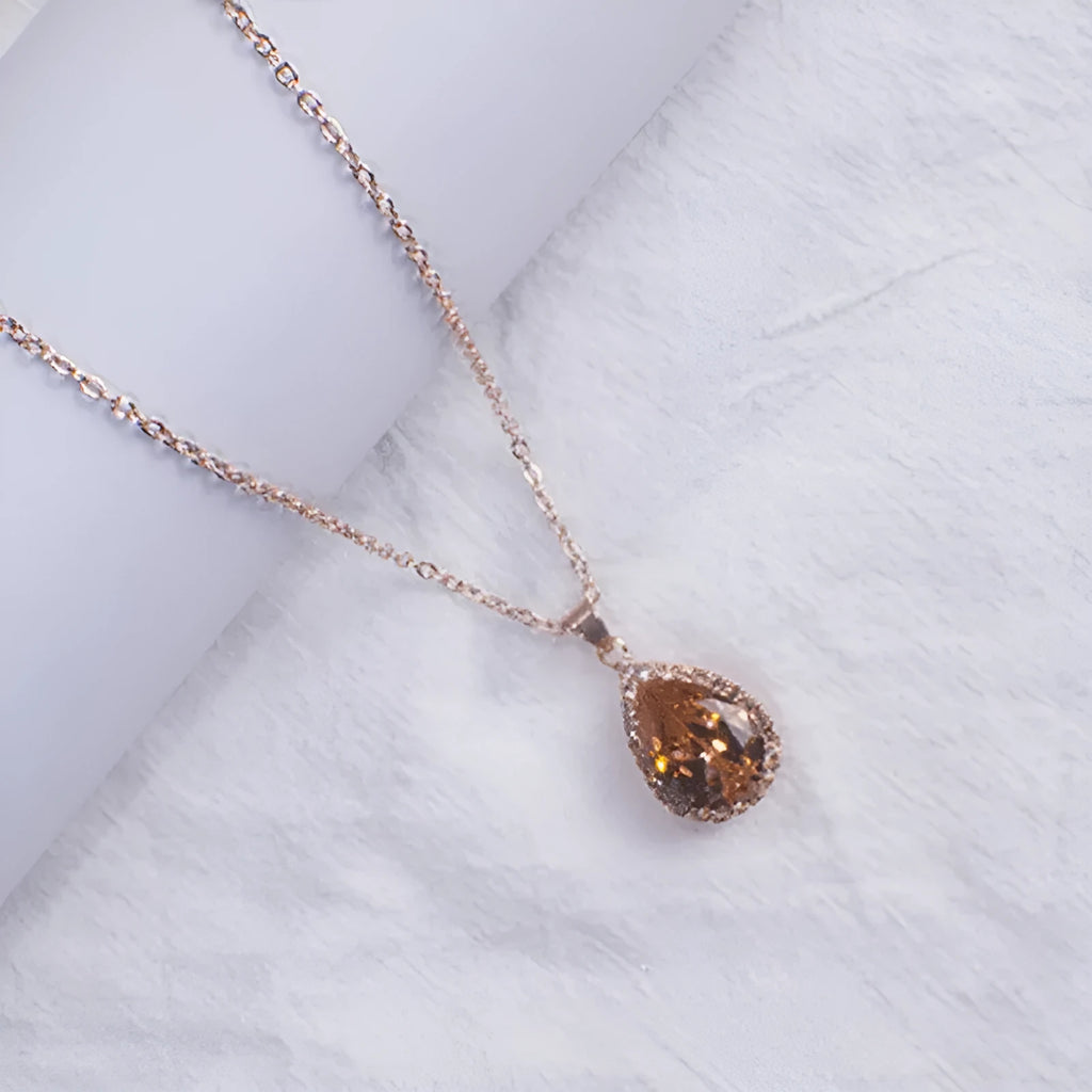 Close-up of a rose gold tone drop shape necklace with rhinestone details on a geometric pendant.