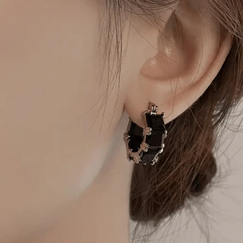 Geometric gold U-shaped hoop earrings with a round black zircon stone, shown from a side view.