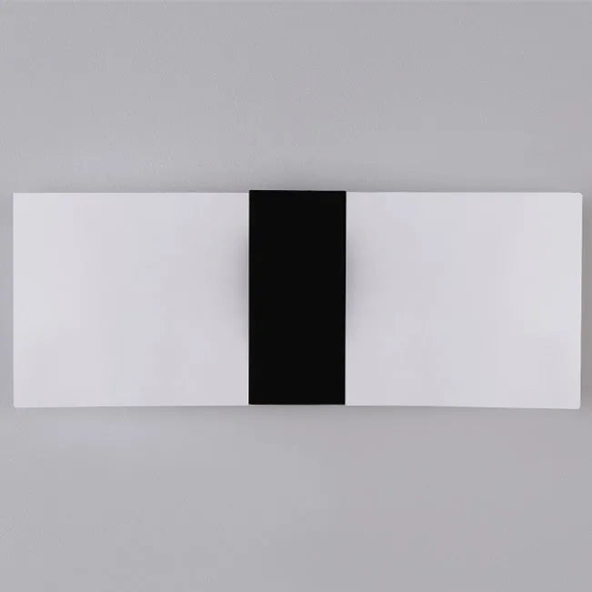 Modern black acrylic LED wall lamp with warm white light on a corridor wall.