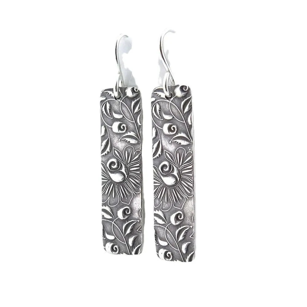 Silver geometric long drop earrings with a carved vine pattern on a white background.
