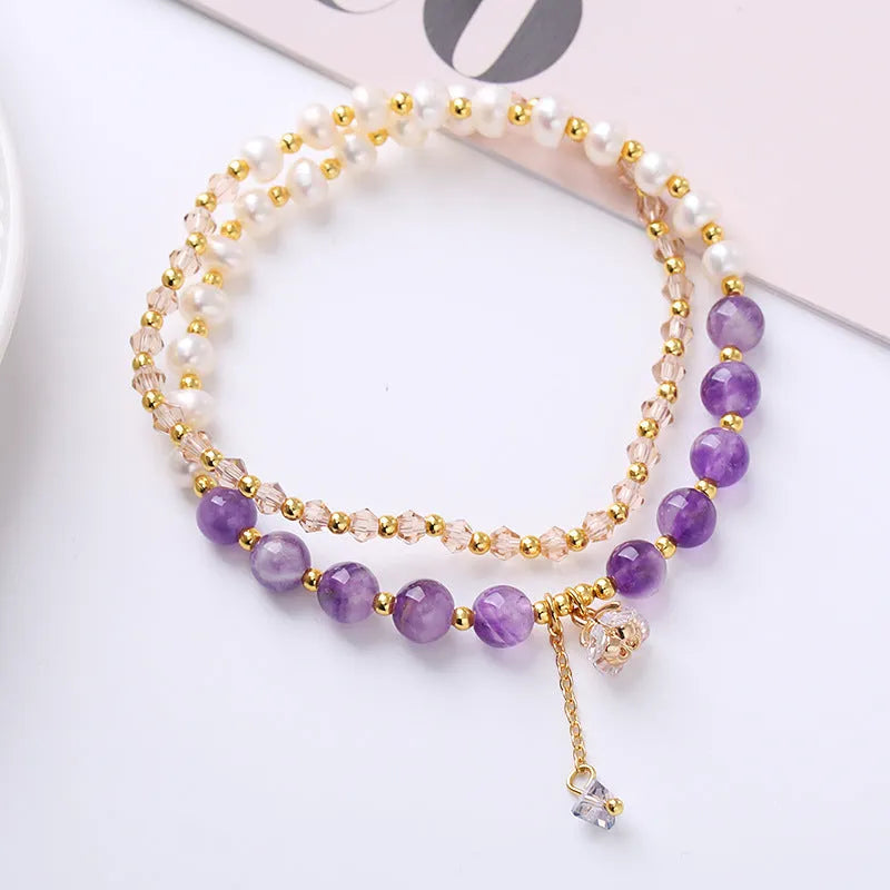 Close-up of a women's double ring bracelet with a freshwater pearl and amethyst crystal beads on a wrist.