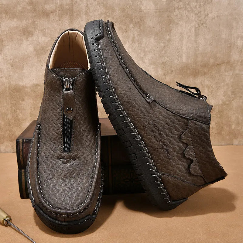 Men's black slip-on loafers with a round toe and sewn rubber sole on a grey background.