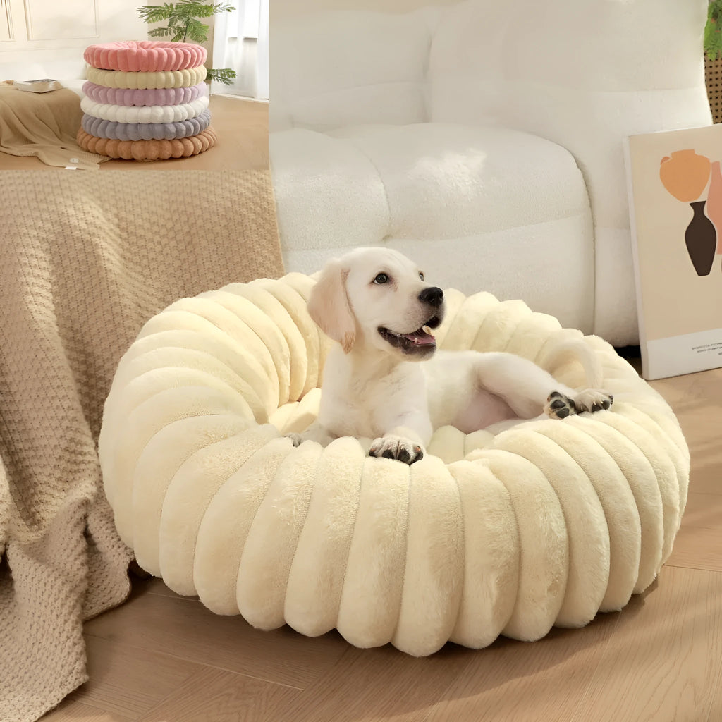 Round beige plush pet bed for a dog, shown in a medium size on a wooden floor.