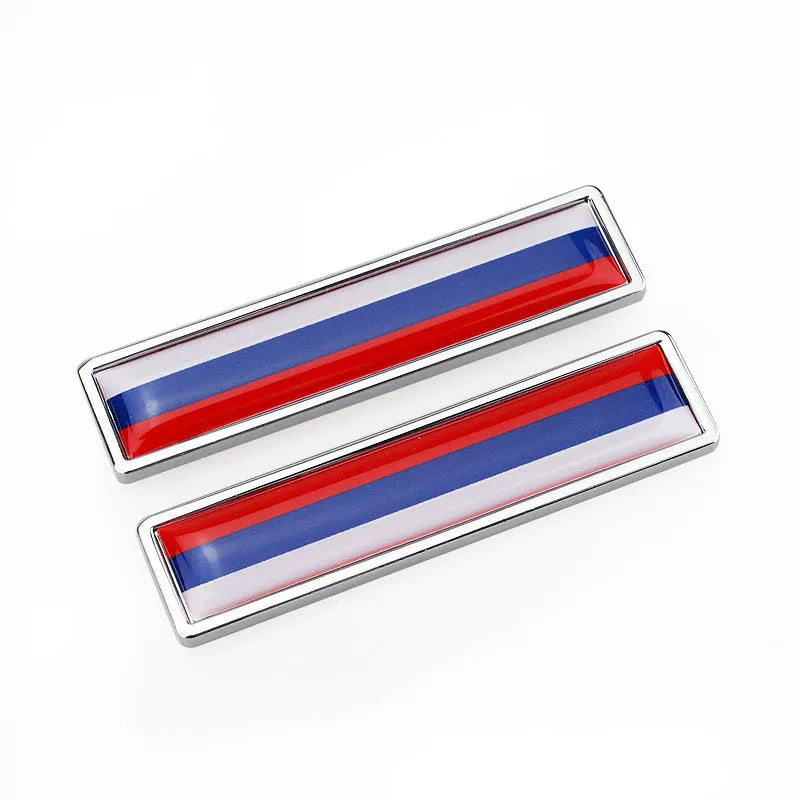 A pair of silver zinc alloy car badge labels with coloured national flag designs, shown at 58mm by 14mm scale.