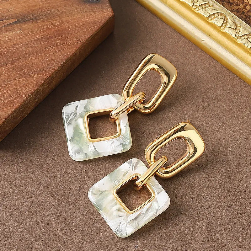 A pair of hollow square geometric earrings with a chamfered edge pattern in a gold tone finish.