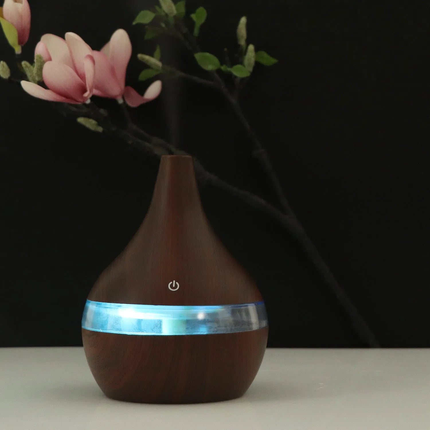 A columnar USB air humidifier with a wood grain finish, remote control, and USB cable on a desktop.