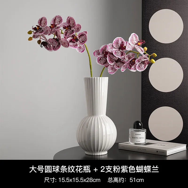 White ceramic ball vase with blue stripes and artificial blue orchid stems on a wooden table.