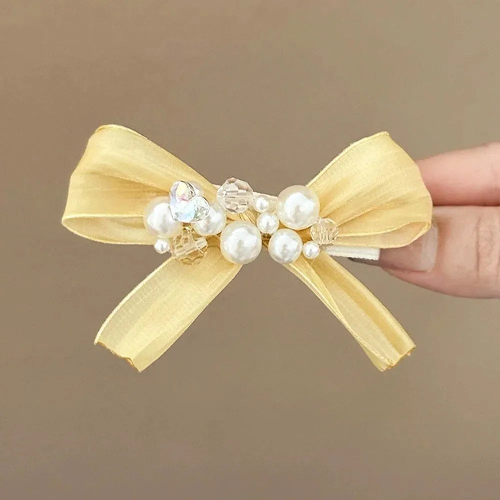 Yellow cloth bow hair clip with pearl accents on a duckbill clip.