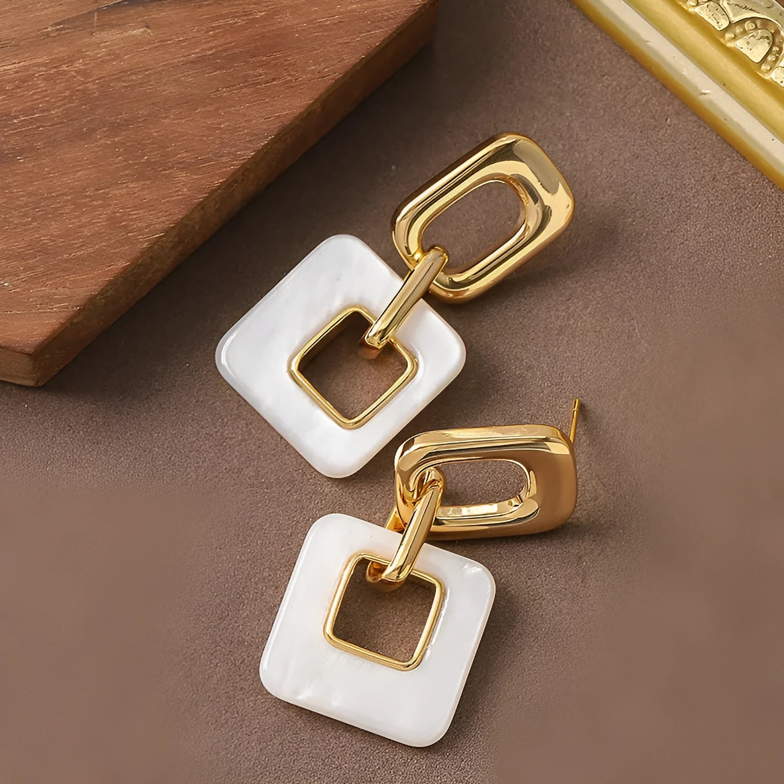 A pair of hollow square geometric earrings with a chamfered edge pattern in a gold tone finish.