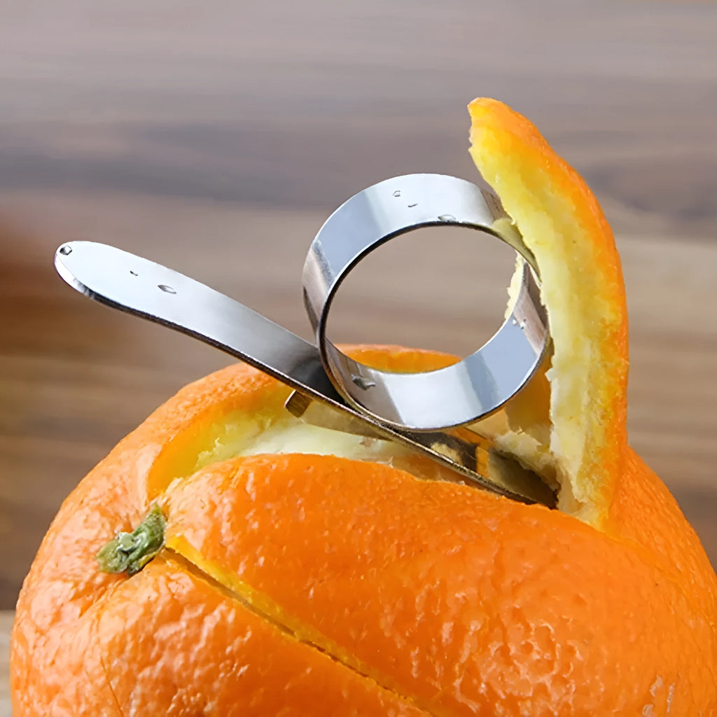 Silver stainless steel fruit peeler ring for oranges, citrus, and pomegranates on a kitchen surface.
