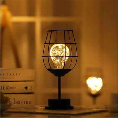 Minimalist hollow wrought iron table lamp in red wine bottle shape with warm white light on a desk