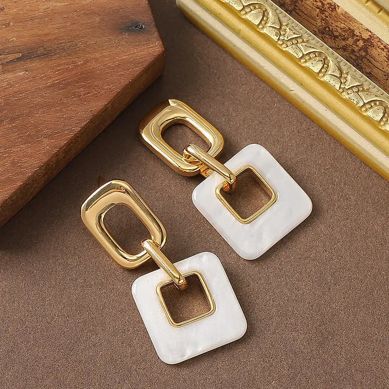A pair of hollow square geometric earrings with a chamfered edge pattern in a gold tone finish.