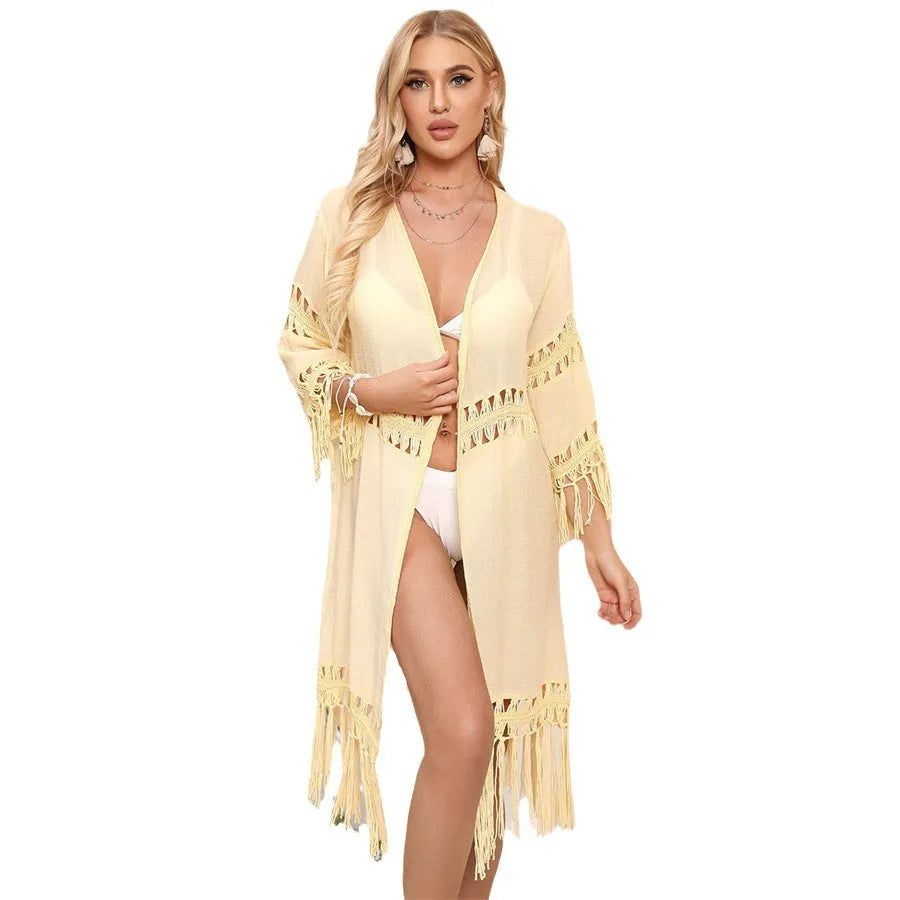 Women's yellow hand-crocheted beach cover-up cardigan with loose stitching and tassels on a hanger.