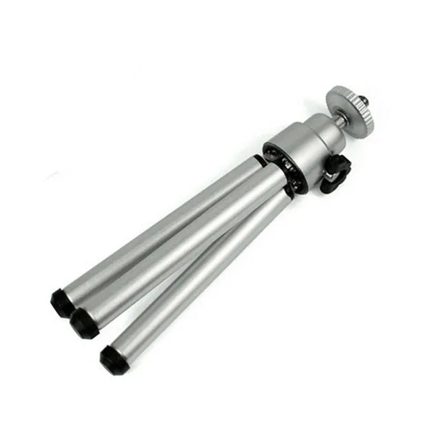 Black mini flexible tripod extended on a table with a silver U-shaped phone clip attached.