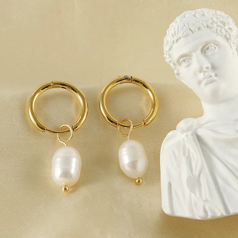 A pair of gold-coloured geometric stud earrings with a central white pearl on a white background.