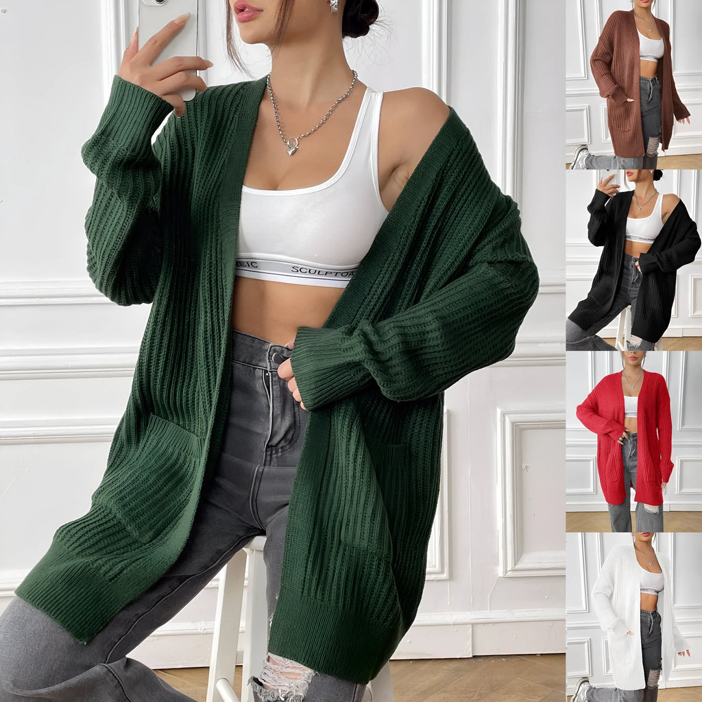 A woman wearing a dark green, loose-fit, mid-length acrylic cardigan with long sleeves and two front pockets.