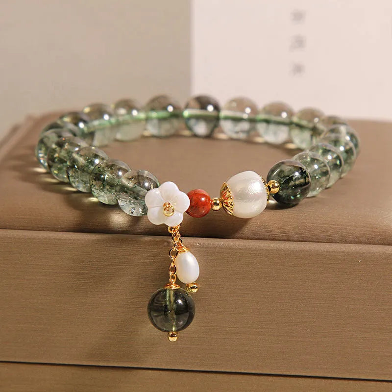 Green phantom quartz crystal bracelet with small shell flower design on woman's wrist.