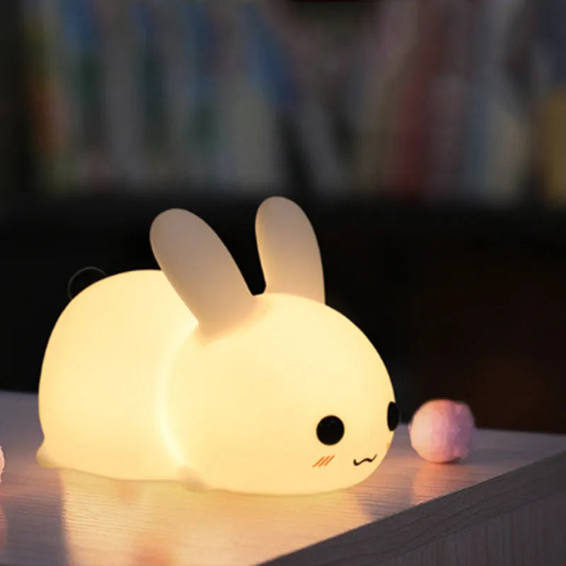 White silicone rabbit night light with warm and white LED glow on a wooden bedside table