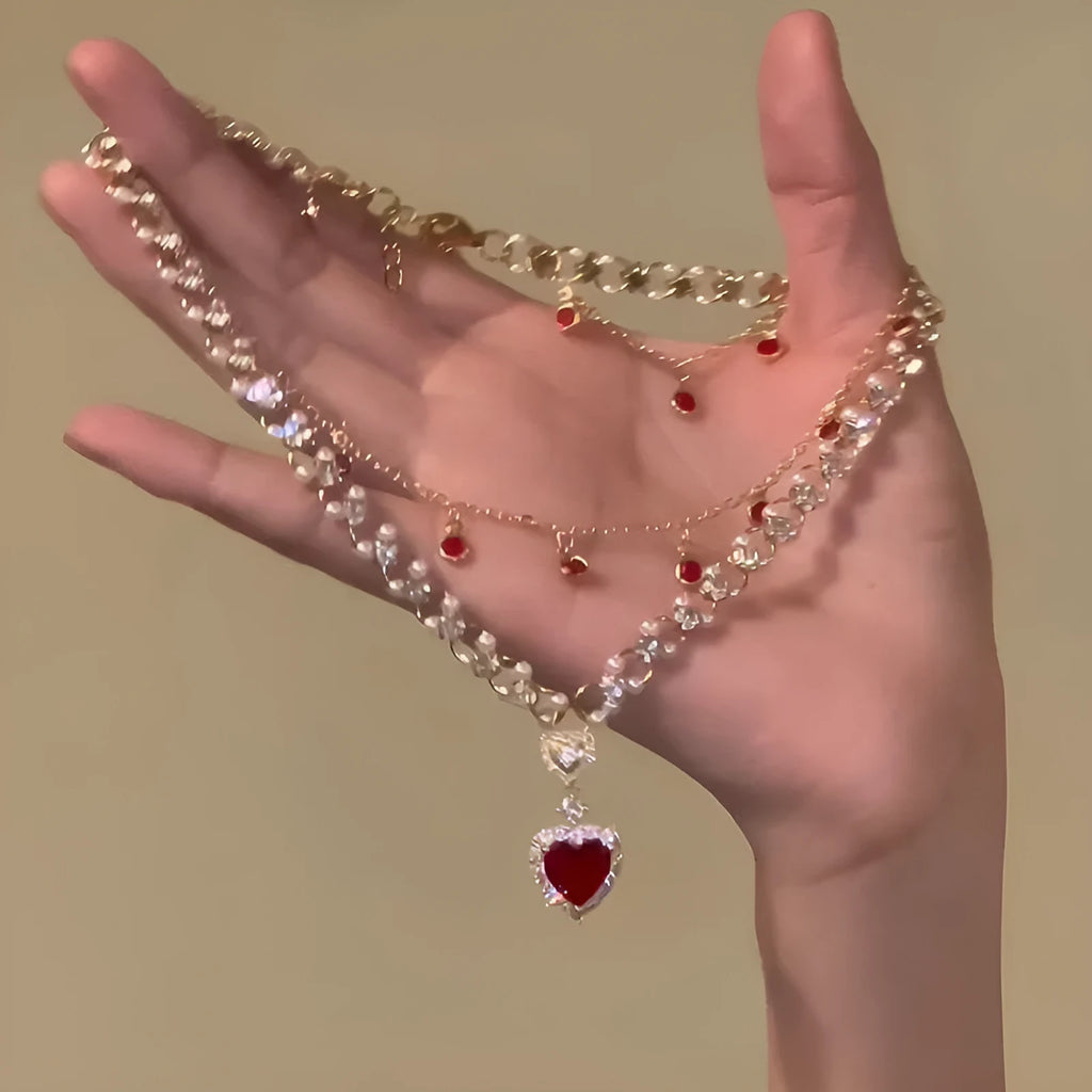Gold tone double chain necklace with a central red love pearl pendant on an adjustable chain.