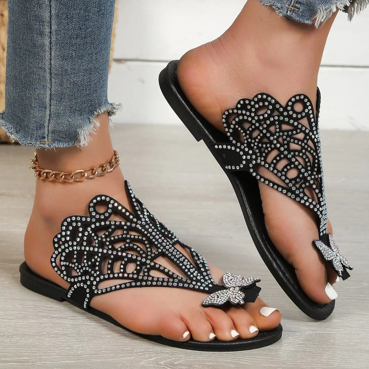Women's black slip-on sandals with rhinestone decoration and hollow-out design on a flat rubber sole.
