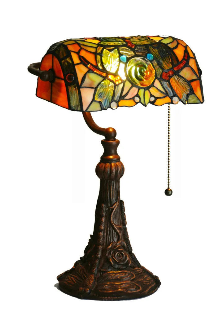 Tiffany stained glass table lamp on a desk, showing its coloured shade and resin base.