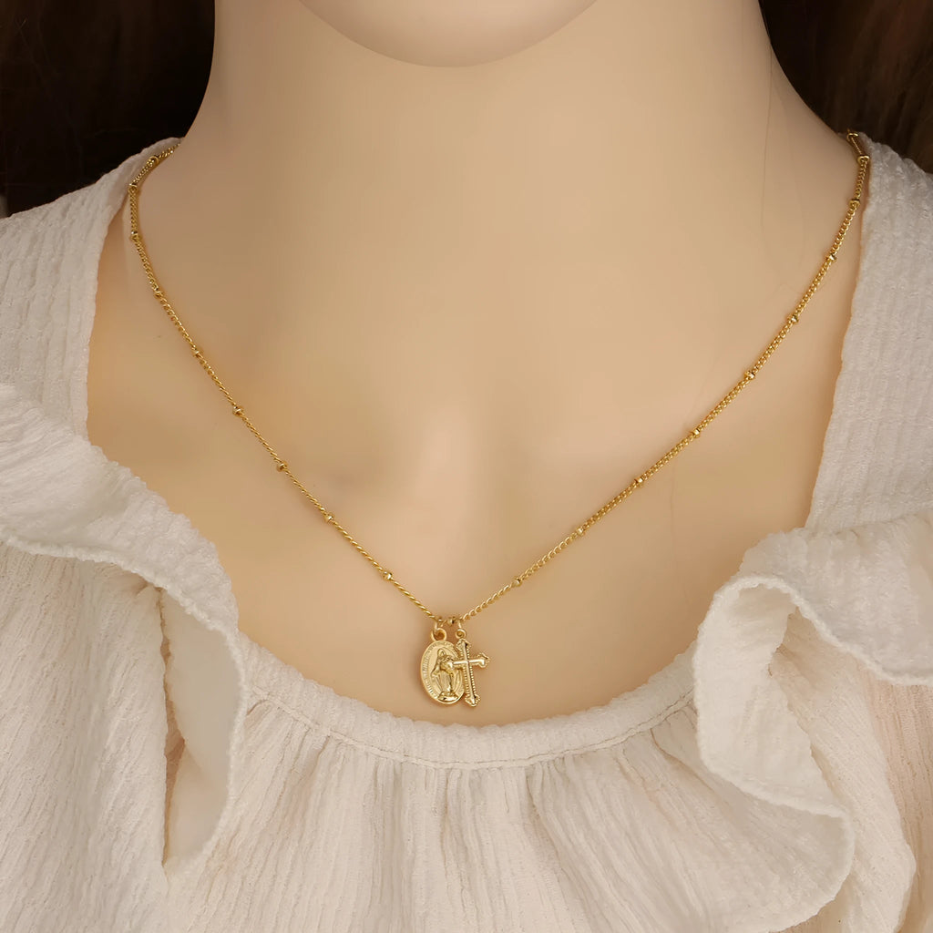 Gold geometric cross necklace with a Virgin Mary ornament pendant on a chain.