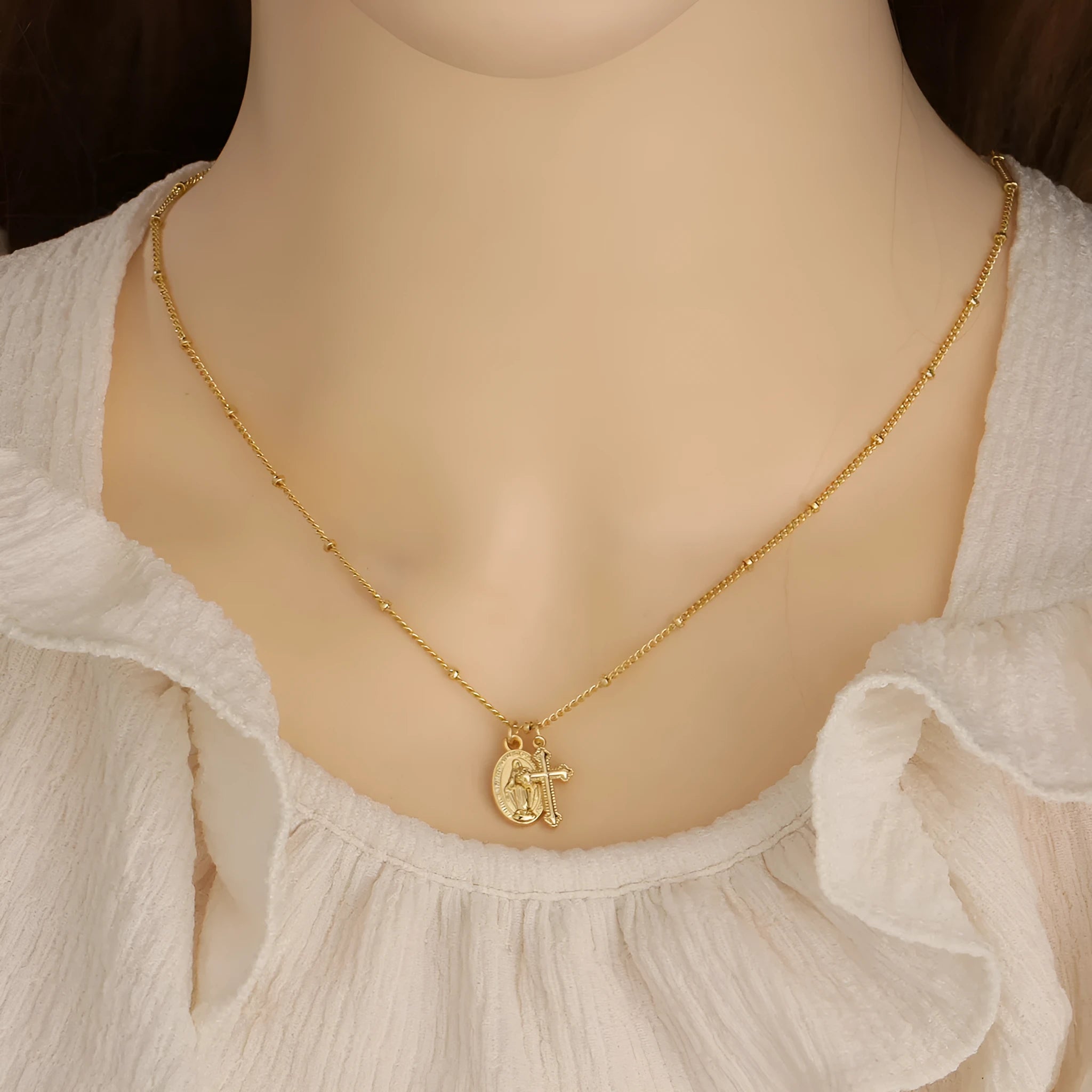 Gold geometric cross necklace with a Virgin Mary ornament pendant on a chain.