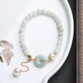 Natural jade bracelet with geometric shape, round pendant, and peace buckle closure on a wrist.