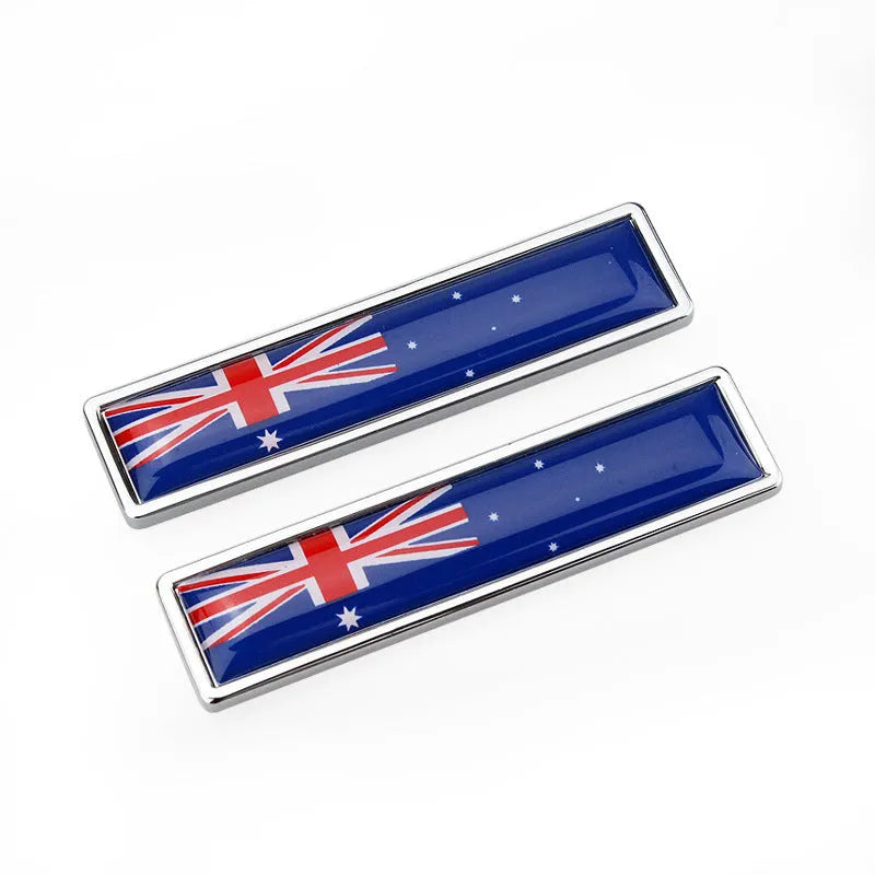 A pair of silver zinc alloy car badge labels with coloured national flag designs, shown at 58mm by 14mm scale.