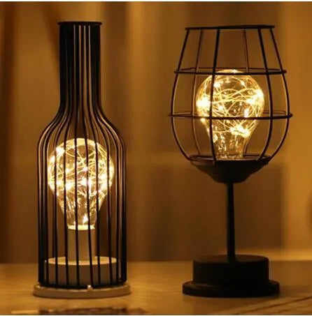 Minimalist hollow wrought iron table lamp in red wine bottle shape with warm white light on a desk