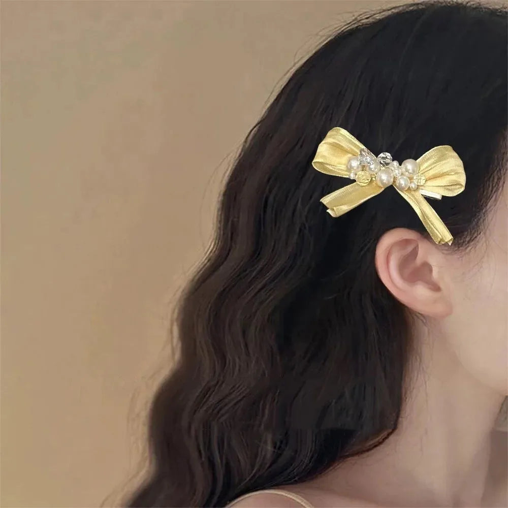 Yellow cloth bow hair clip with pearl accents on a duckbill clip.