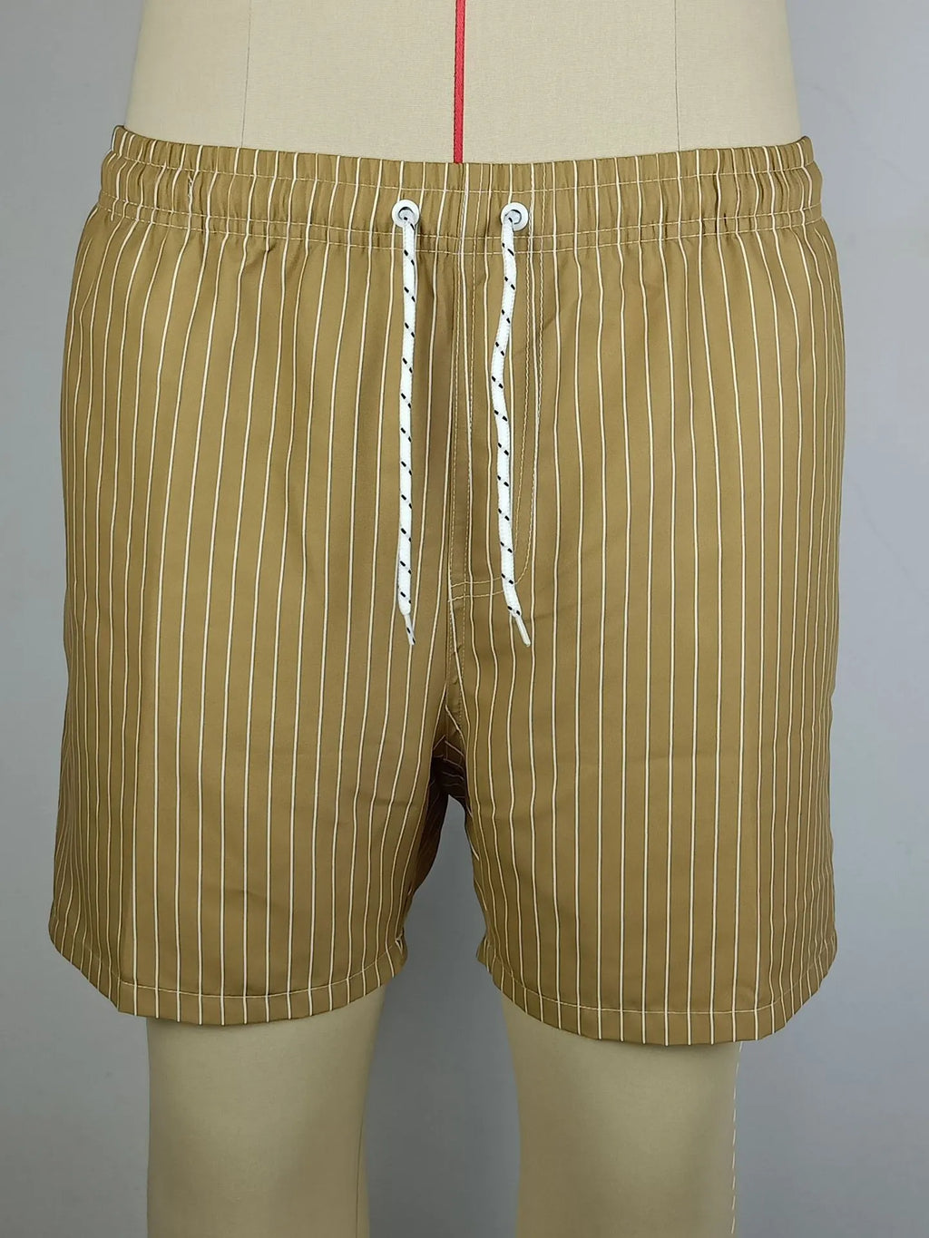 Men's striped polyester shorts in light blue, shown on a beach.