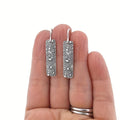 Silver geometric long drop earrings with a carved vine pattern on a white background.