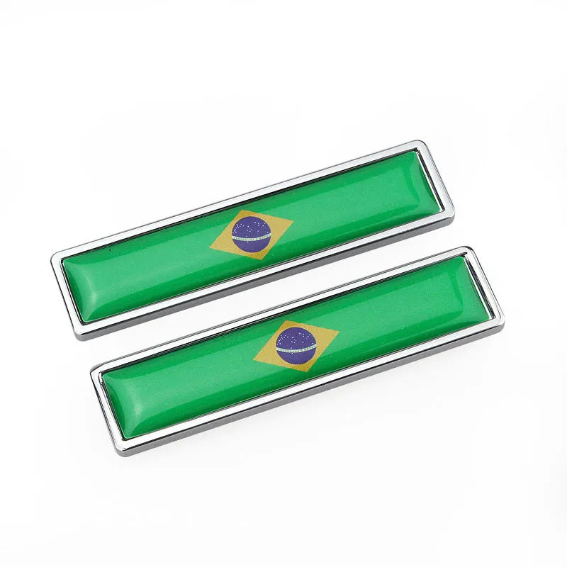 A pair of silver zinc alloy car badge labels with coloured national flag designs, shown at 58mm by 14mm scale.