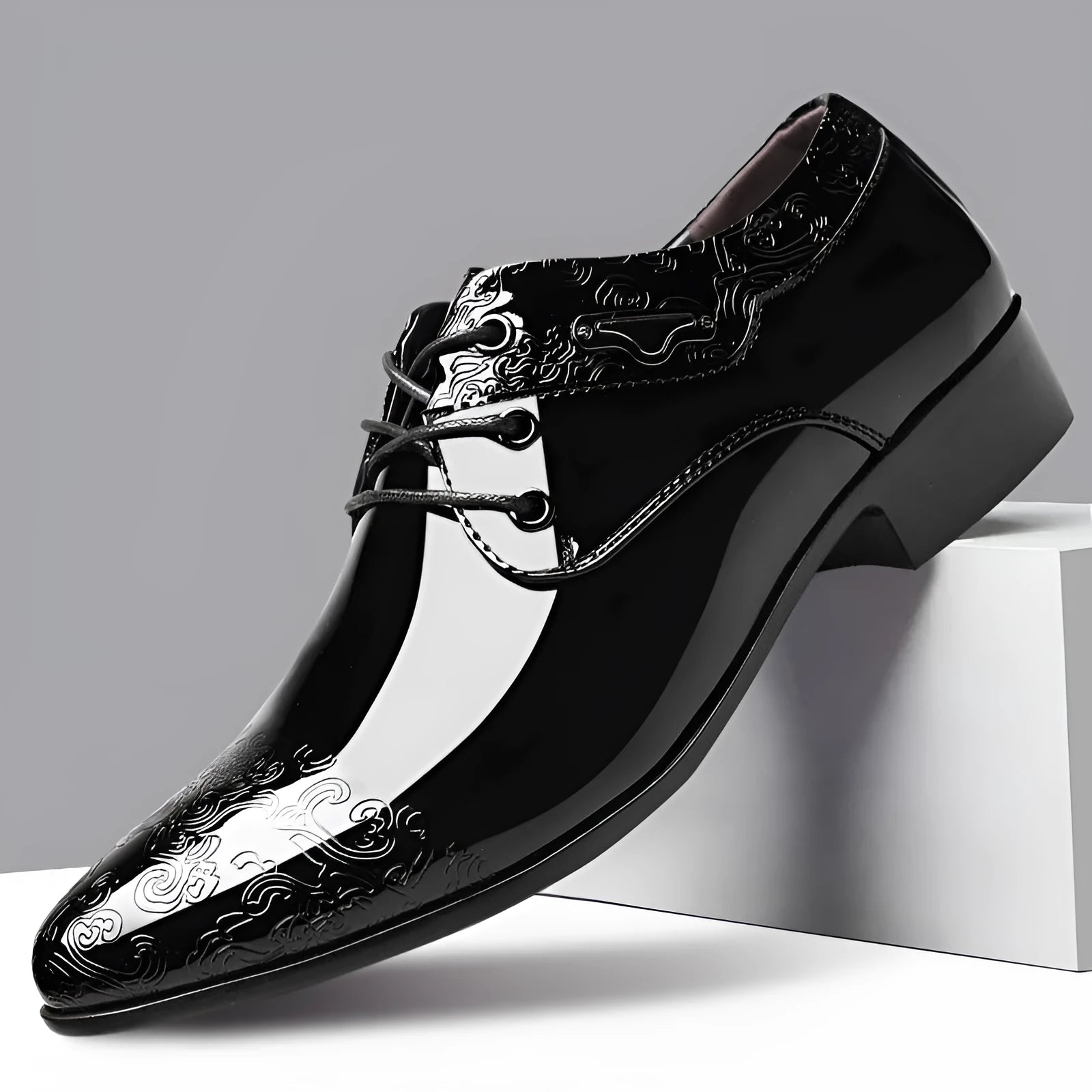 Glossy black men's business formal shoes with patent finish, pointed toe, and carved detail on a neutral background