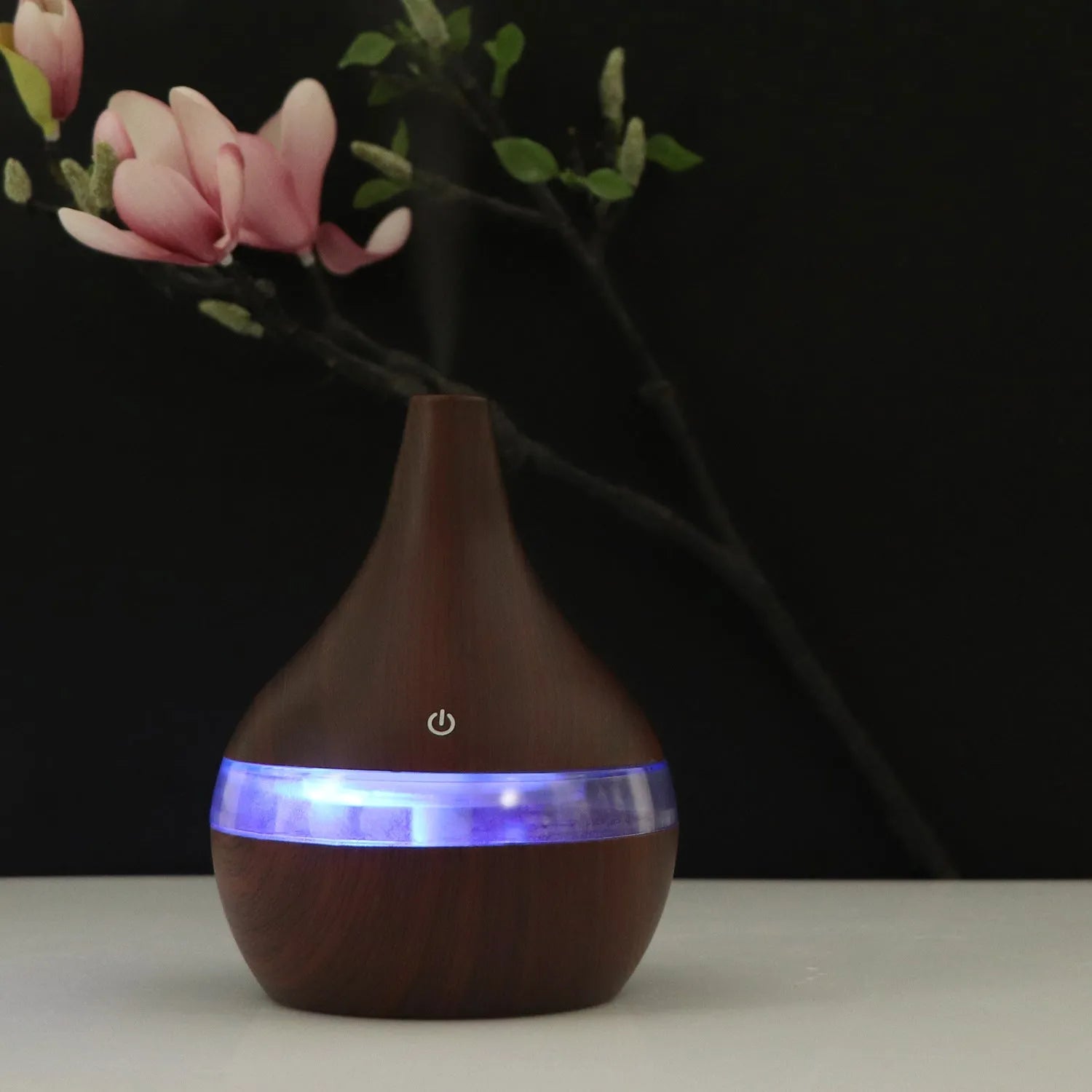 A columnar USB air humidifier with a wood grain finish, remote control, and USB cable on a desktop.