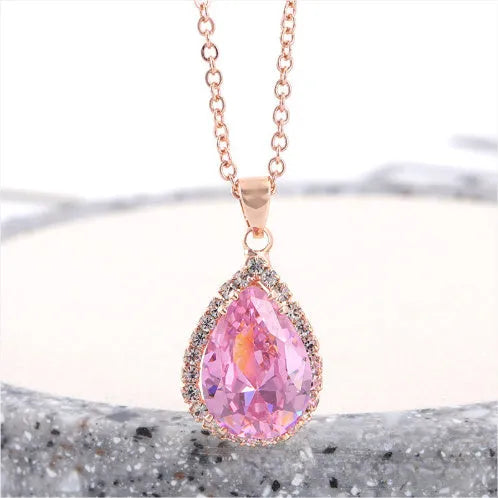 Close-up of a rose gold tone drop shape necklace with rhinestone details on a geometric pendant.