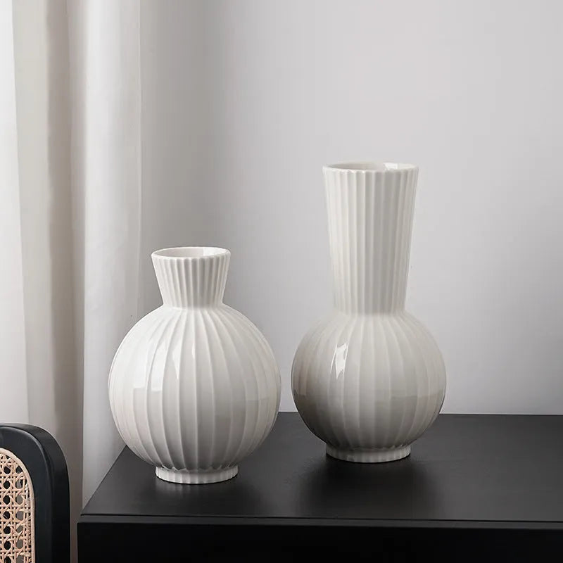 White ceramic ball vase with blue stripes and artificial blue orchid stems on a wooden table.