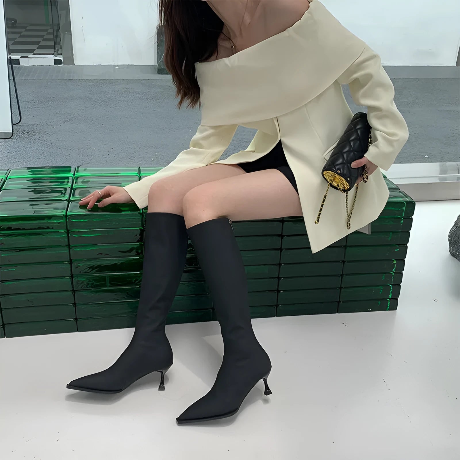 Black women's pointed toe below-the-knee boots with a stiletto heel and back zipper on a plain background.