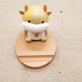 Carved beech wood phone stand with a detailed resin decorative topper, holding a mobile phone upright on a desk.
