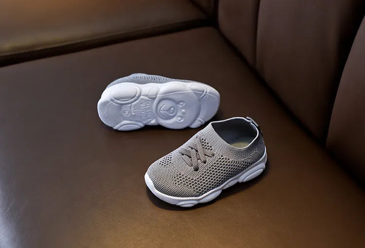 Children's fabric lazy shoe with a non-slip rubber sole, shown in colour options of white, black, pink, and grey.