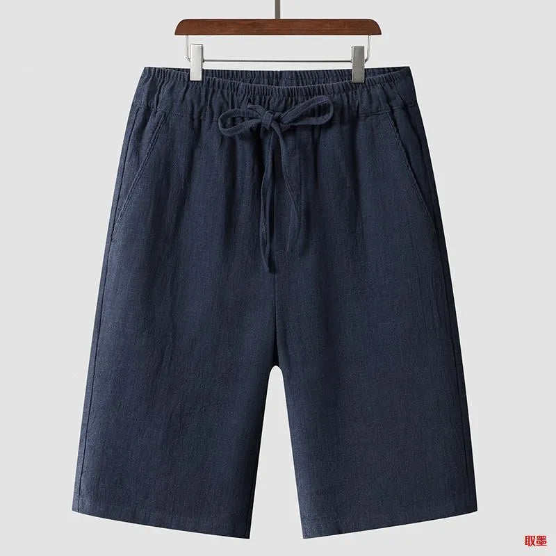 Men's beige linen shorts with loose cropped leg and elasticated waistband on a neutral background.